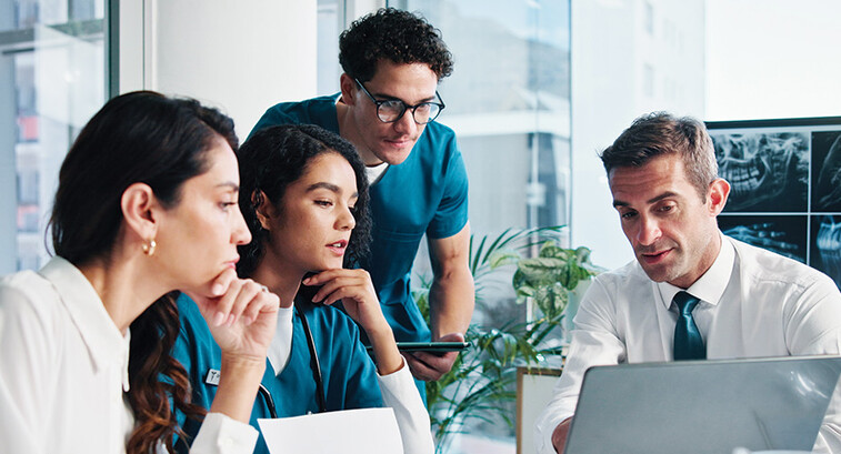 medical and IT team collaborate at table in front of laptop