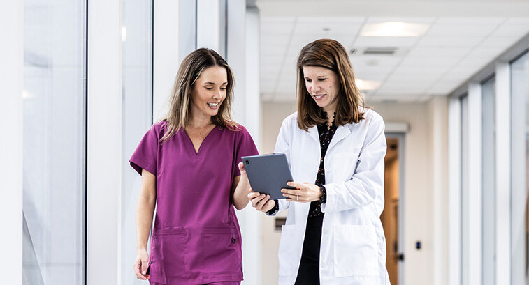 two clinicians walking down hallway looking at a tablet