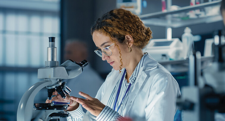 healthcare researcher looks through microscope in dark lab