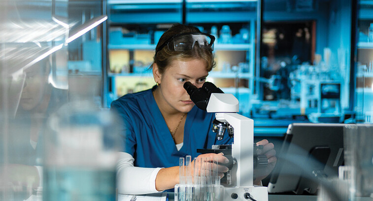 scientist looks through microscope in lab