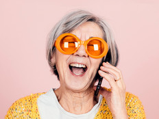 older adult woman wearing sunglasses laughs while on a smart phone