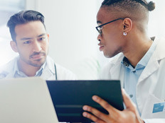 two doctors discuss treatment plans over laptop and tablet