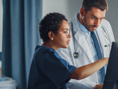 nurse and physician collaborate over desktop computer in patient room