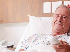 man in hospital bed uses remote to watch tv