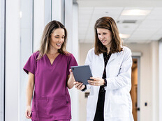 two clinicians walking down hallway looking at a tablet