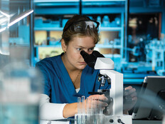scientist looks through microscope in lab