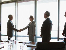 business people gather around conference table as leaders shake hands