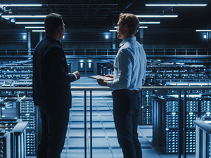 two IT professionals stand over server room