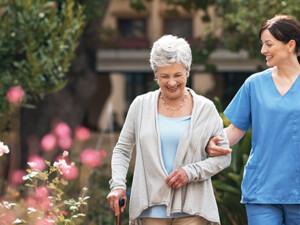 nurse walks with senior woman through a garden