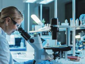 scientist looks through microscope in lab