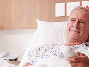 man in hospital bed uses remote to watch tv