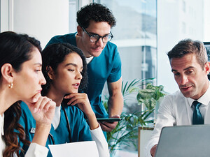 medical and IT team collaborate at table in front of laptop