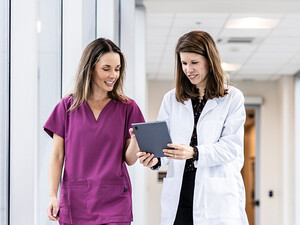 two clinicians walking down hallway looking at a tablet
