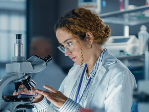 healthcare researcher looks through microscope in dark lab