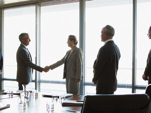 business people gather around conference table as leaders shake hands
