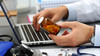 Male medicine doctor hands hold jar of pills and type something on laptop computer keyboard.