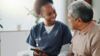 nurse and older adult talk on couch with tablet