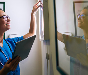 Side view of smiling middle aged nurse checking X-ray in a doctors office.