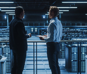 two IT professionals stand over server room