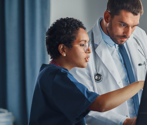 nurse and physician collaborate over desktop computer in patient room