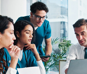 medical and IT team collaborate at table in front of laptop