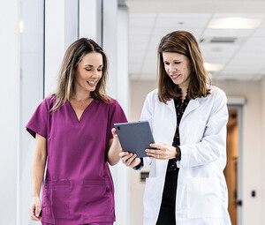 two clinicians walking down hallway looking at a tablet
