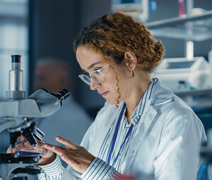 healthcare researcher looks through microscope in dark lab