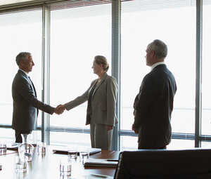 business people gather around conference table as leaders shake hands